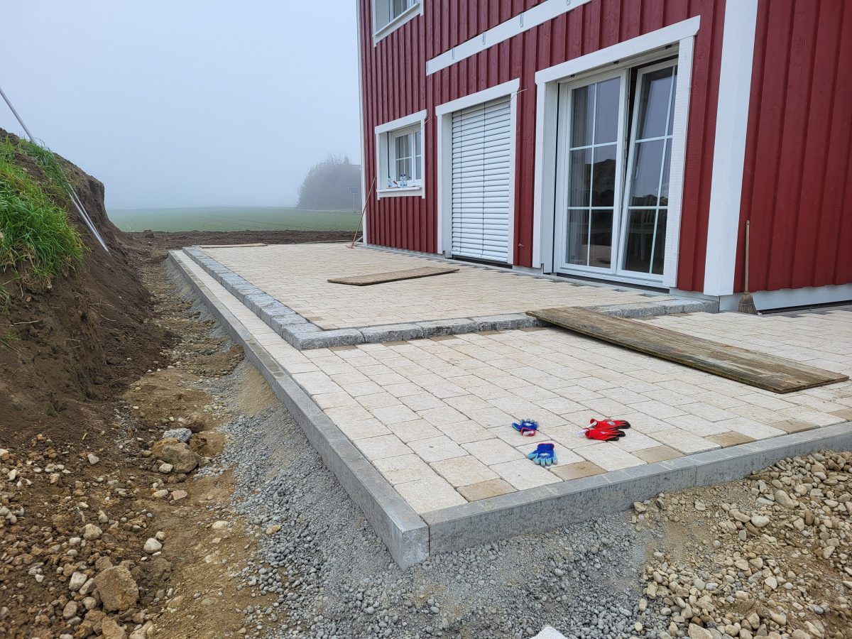 Frisch gepflasterte Terrasse an einem Wohnhaus, Baustelle drumherum