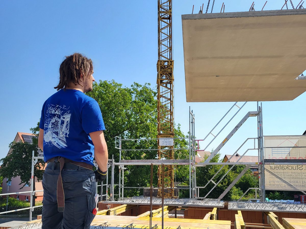 Mitarbeiter beobachtet, wie ein Betonfertigteil für die Geschossdecke am Kran einschwebt