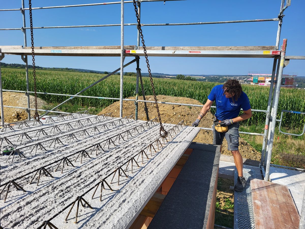 Mitarbeiter führt ein Betonfertigteil für die Geschossdecke am Kran ein